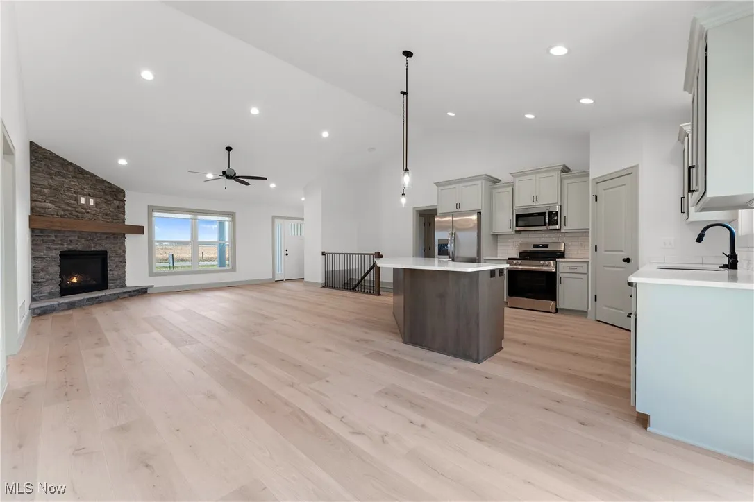 Kitchen featuring sink, appliances with stainless steel finishes, decorative light fixtures, a kitchen island, and light wood-type flooring