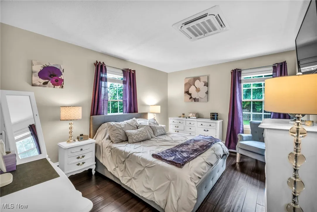 Bedroom with multiple windows, dark wood-style floors, and cooling unit