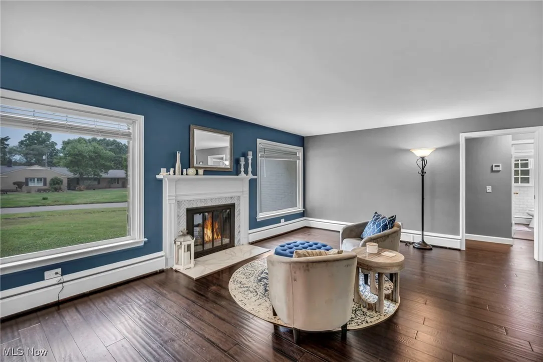 Living room with a baseboard heating unit, a fireplace, hardwood / wood-style flooring, and baseboard heating