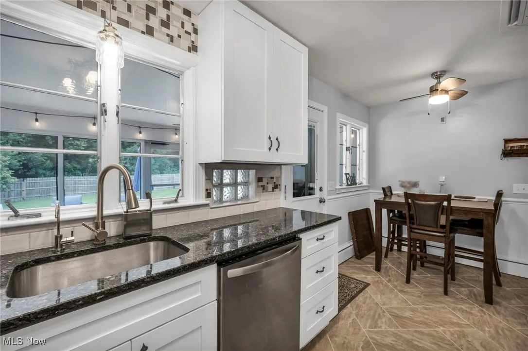 Kitchen with dishwasher, white cabinets, a ceiling fan, dark stone counters, and backsplash