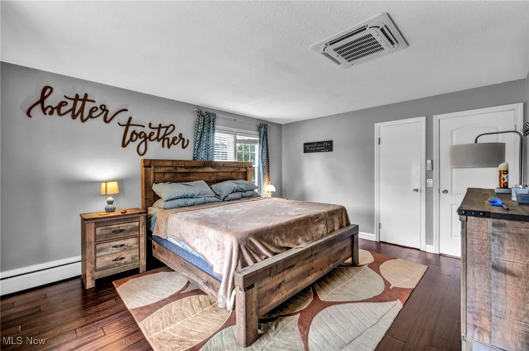 Bedroom with a baseboard heating unit, wood-type flooring, a textured ceiling, and cooling unit
