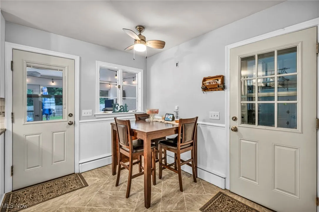 Dining area with ceiling fan, a baseboard heating unit, wainscoting, a decorative wall, and light marble finish flooring