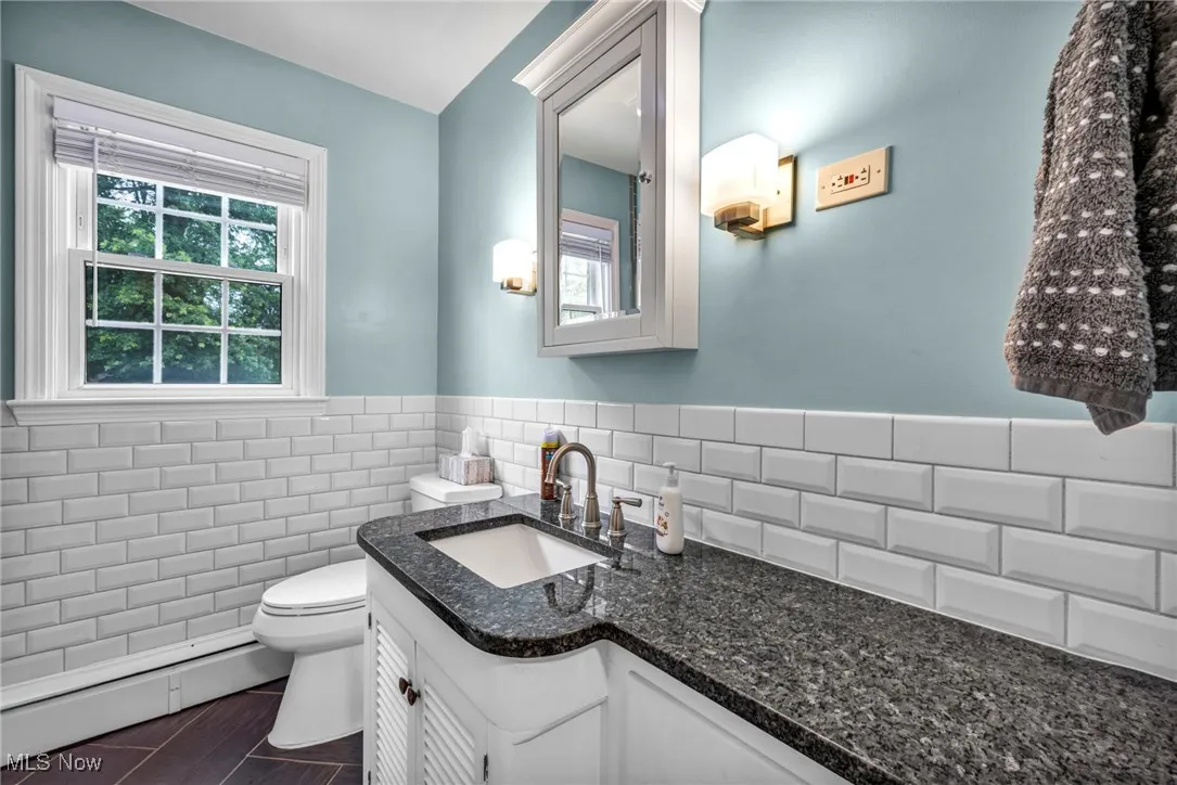 Bathroom with a baseboard radiator, vanity, tile walls, and a wainscoted wall