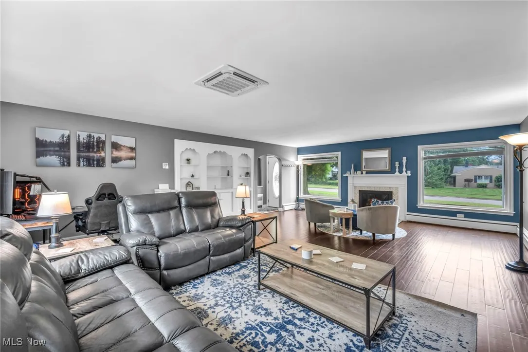 Living area with arched walkways, a baseboard radiator, hardwood / wood-style flooring, built in features, and a fireplace