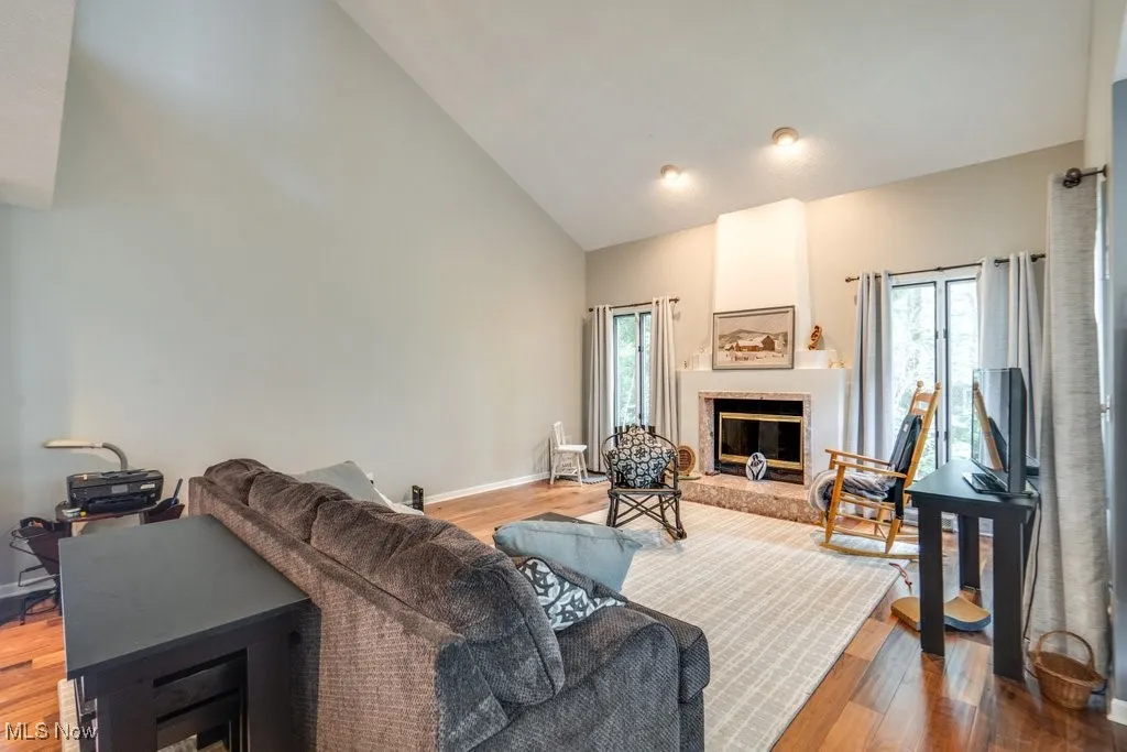 Living room with high vaulted ceiling, plenty of natural light, a fireplace, and wood finished floors