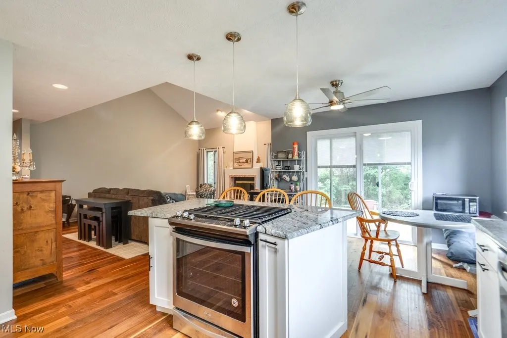 Kitchen with stainless steel range with gas stovetop, light wood-type flooring, open floor plan, a ceiling fan, and light stone counters