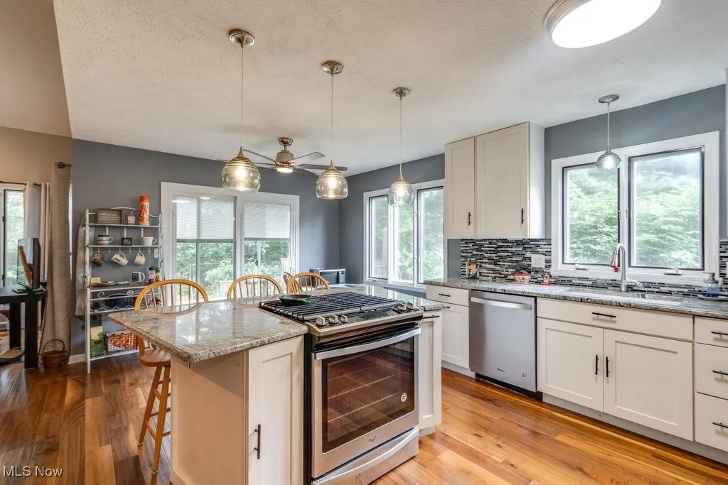 Kitchen with appliances with stainless steel finishes, light wood-type flooring, tasteful backsplash, light stone countertops, and white cabinetry