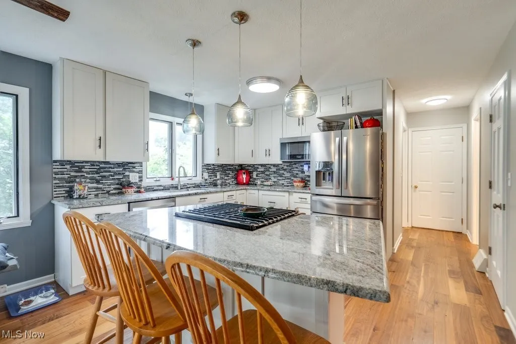 Kitchen featuring appliances with stainless steel finishes, a kitchen breakfast bar, tasteful backsplash, light wood-style flooring, and white cabinetry