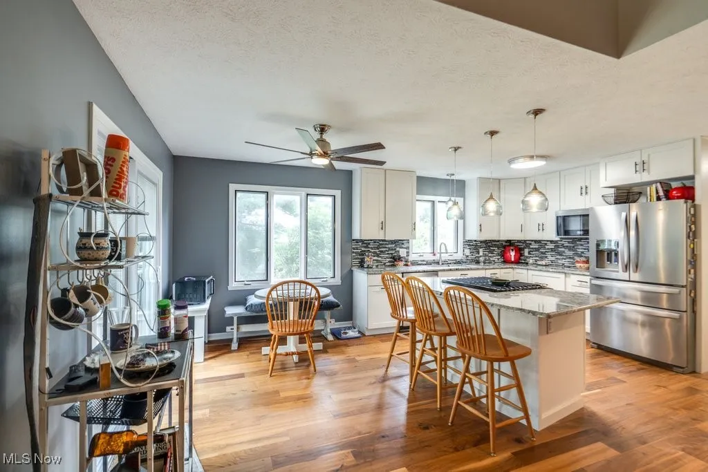 Kitchen featuring appliances with stainless steel finishes, decorative backsplash, a textured ceiling, light wood-style floors, and white cabinetry