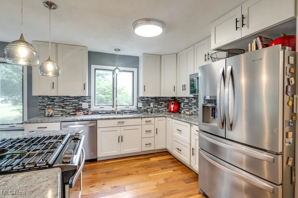 Kitchen featuring appliances with stainless steel finishes, decorative backsplash, white cabinetry, and light wood-style floors