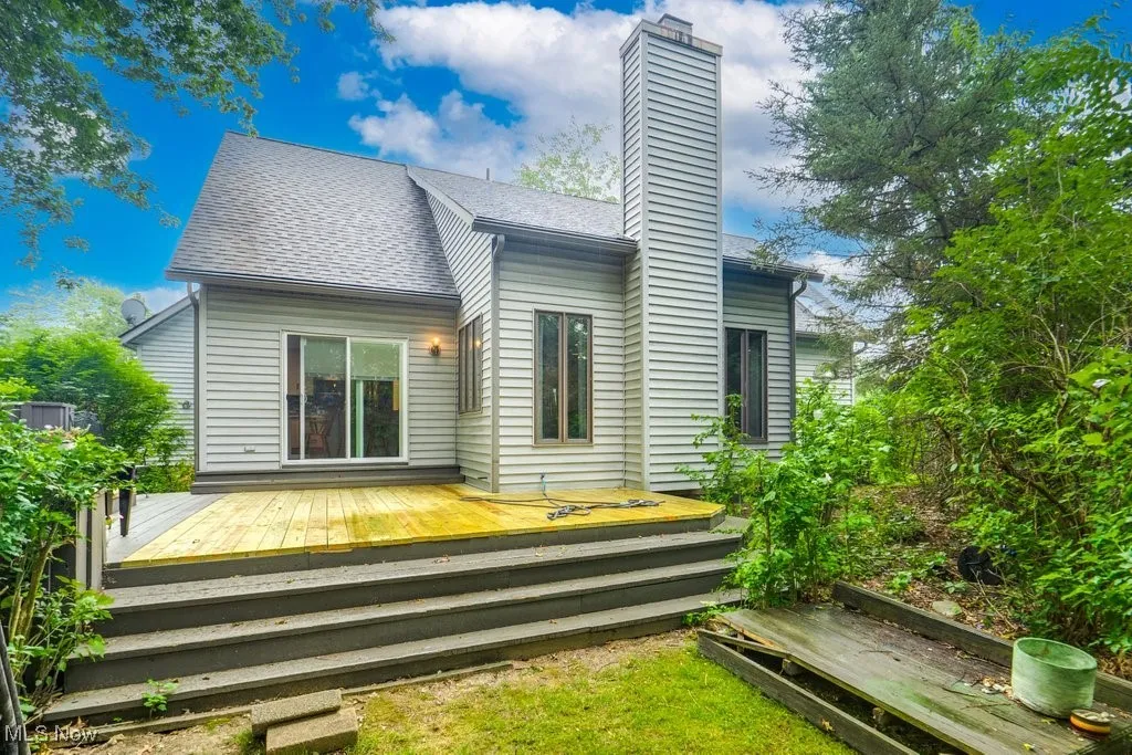 Rear view of house featuring a shingled roof, a chimney, and a deck
