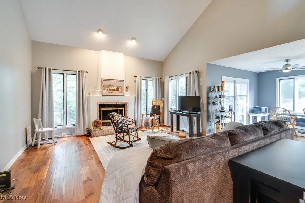 Living room featuring a fireplace, light wood-type flooring, high vaulted ceiling, and ceiling fan