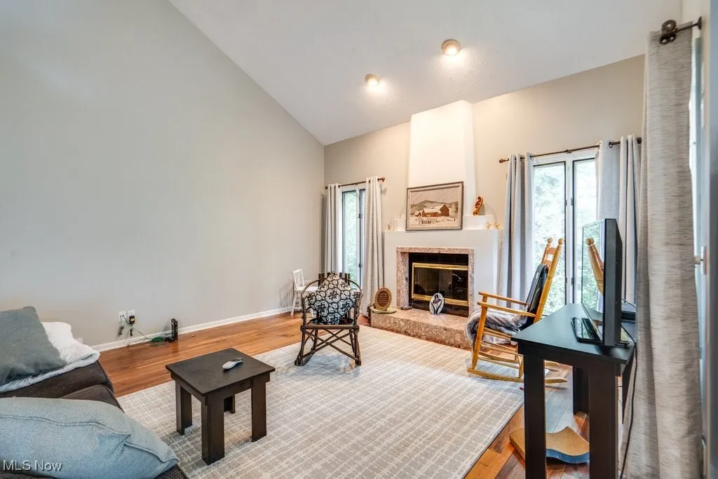 Living area featuring plenty of natural light, high vaulted ceiling, wood finished floors, and a large fireplace