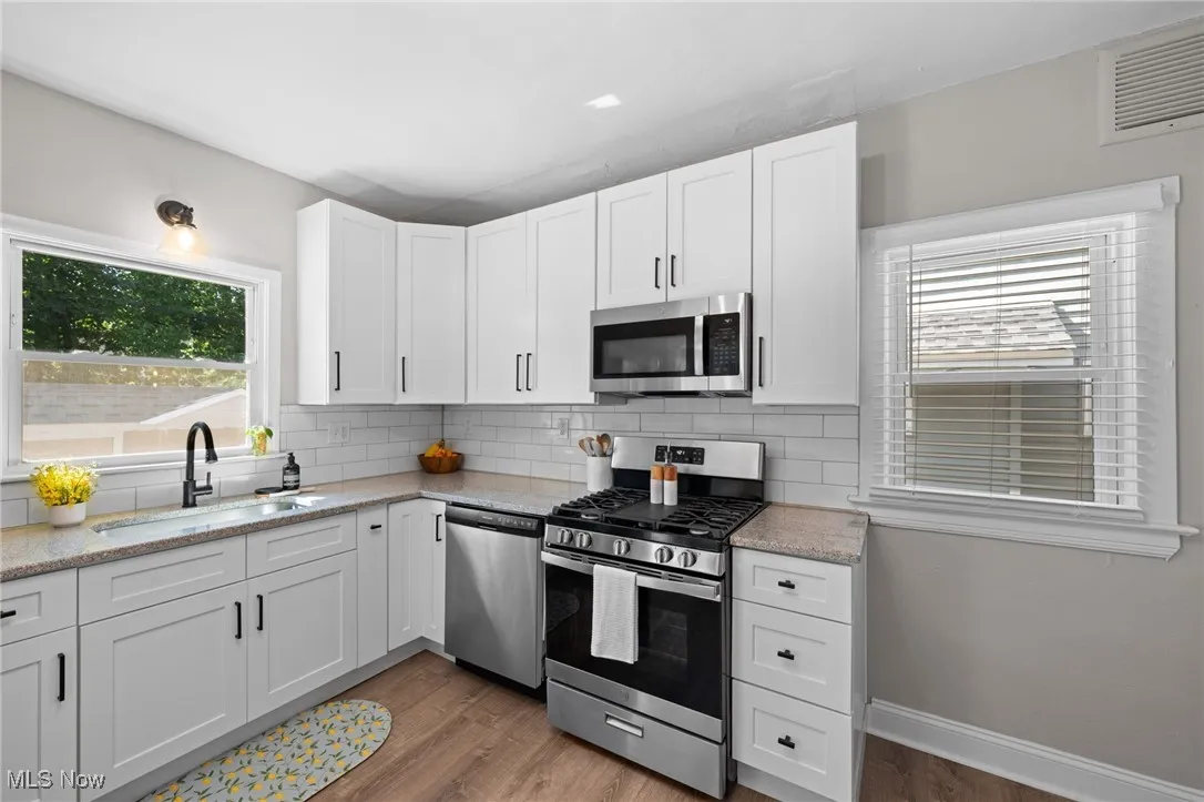 Kitchen with stainless steel appliances, backsplash, light wood-type flooring, and white cabinets