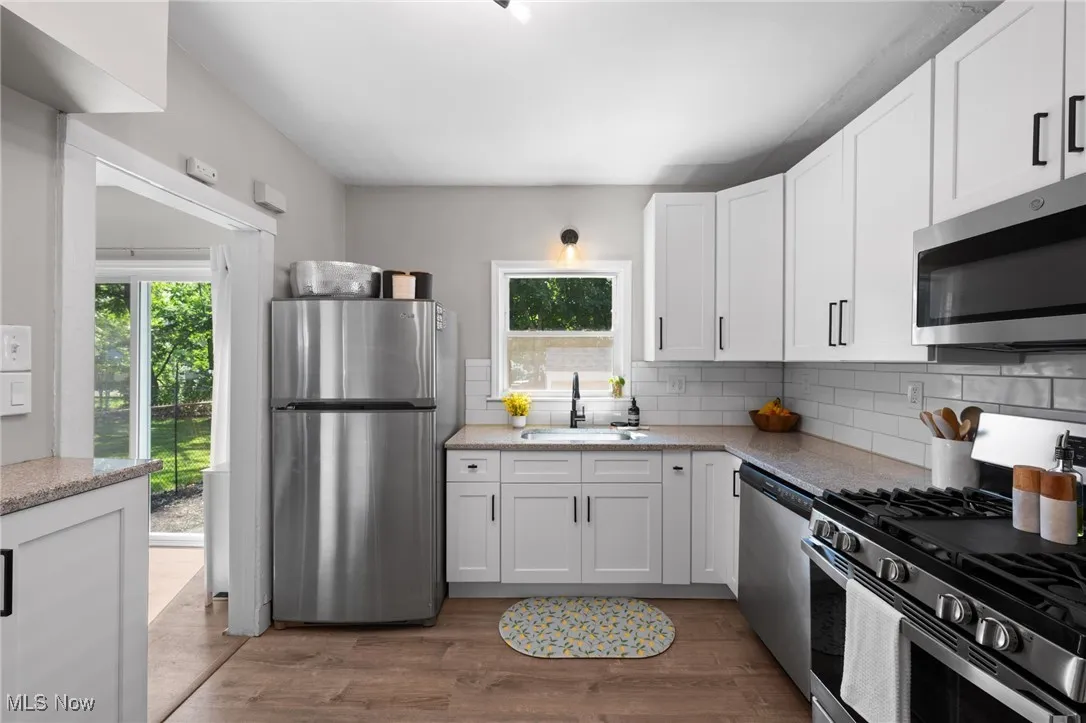 Kitchen with appliances with stainless steel finishes, healthy amount of natural light, backsplash, and white cabinetry