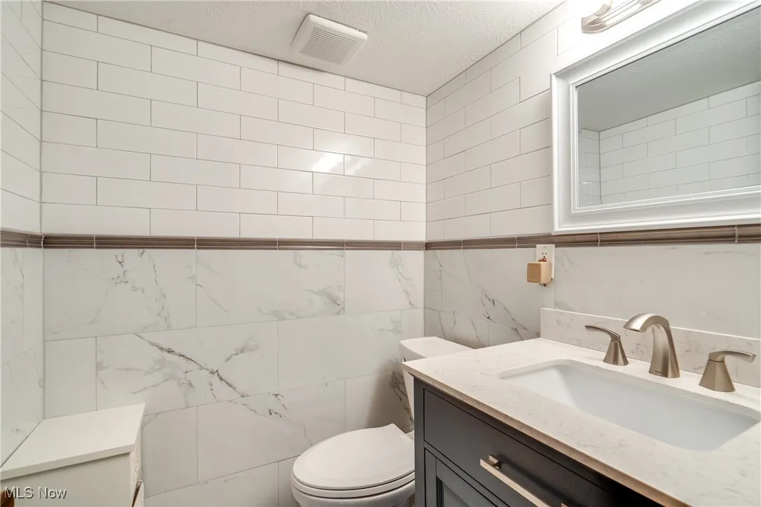 Half bath featuring tile walls, vanity, and a textured ceiling