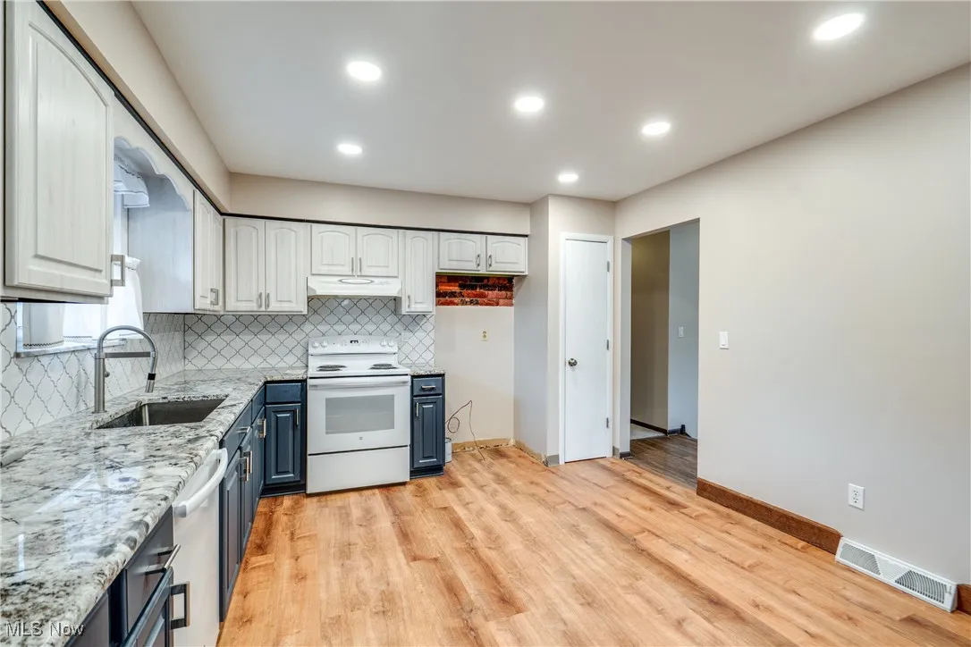 Kitchen with white electric range oven, decorative backsplash, light stone countertops, light wood-type flooring, and recessed lighting