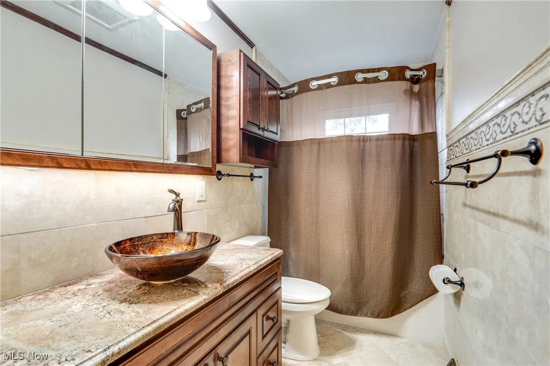 Bathroom with vanity, shower / bath combo, tile walls, and tasteful backsplash