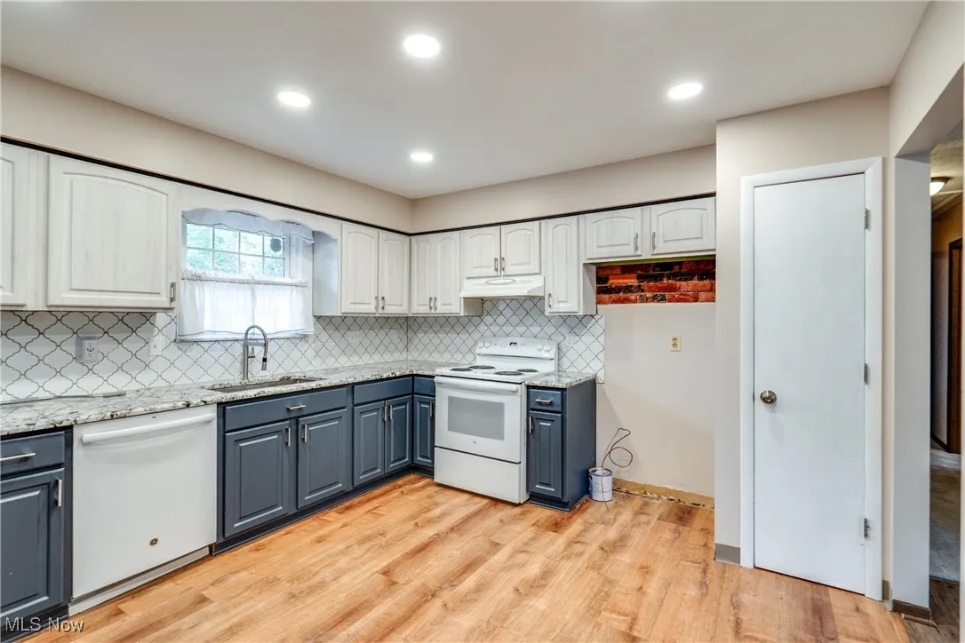 Kitchen with white appliances, backsplash, light wood-type flooring, white cabinets, and recessed lighting