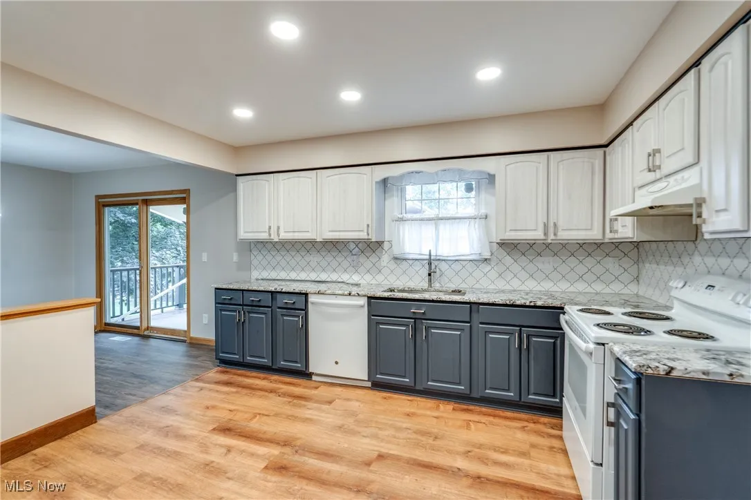 Kitchen featuring white appliances, gray cabinetry, light wood-style flooring, under cabinet range hood, and white cabinetry