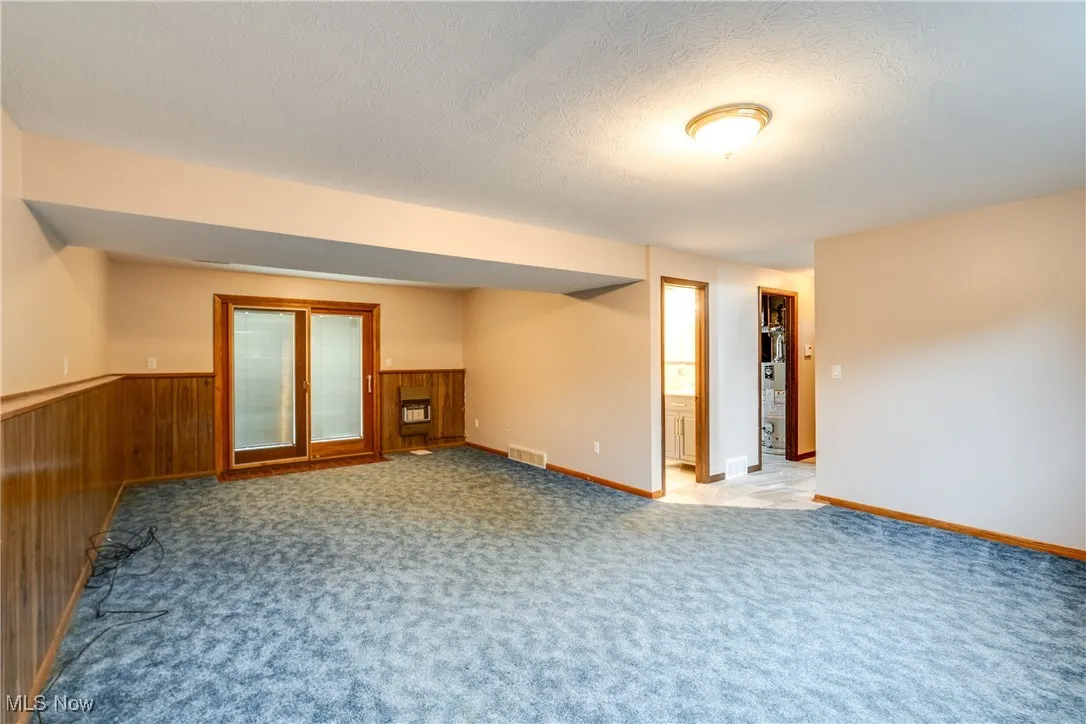 Unfurnished room featuring a textured ceiling, wainscoting, light carpet, and wood walls