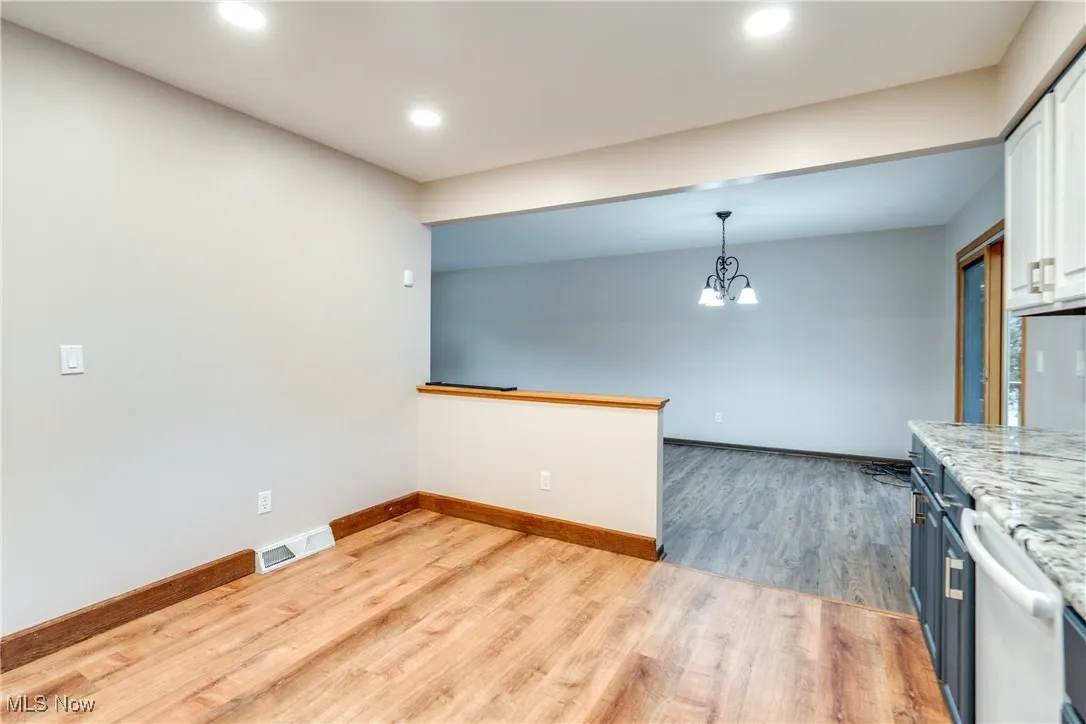 Kitchen with light wood-type flooring, a chandelier, white cabinets, recessed lighting, and light stone countertops
