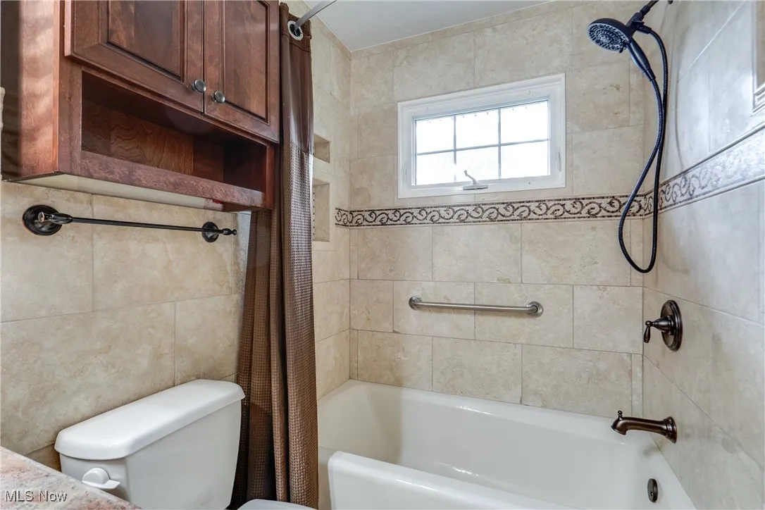Full bathroom featuring shower / bathtub combination with curtain and toilet