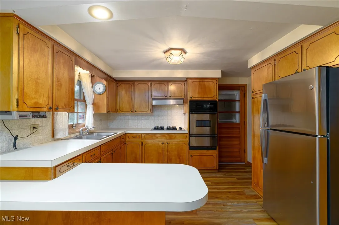 Breakfast bar with stainless steel wall oven, cooktop, exhaust hood and fridge