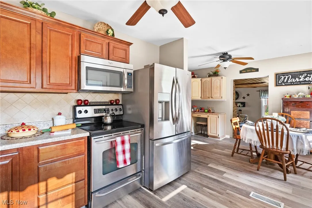 Kitchen featuring ceiling fan, stainless steel appliances, light wood-style flooring, light countertops, and backsplash
