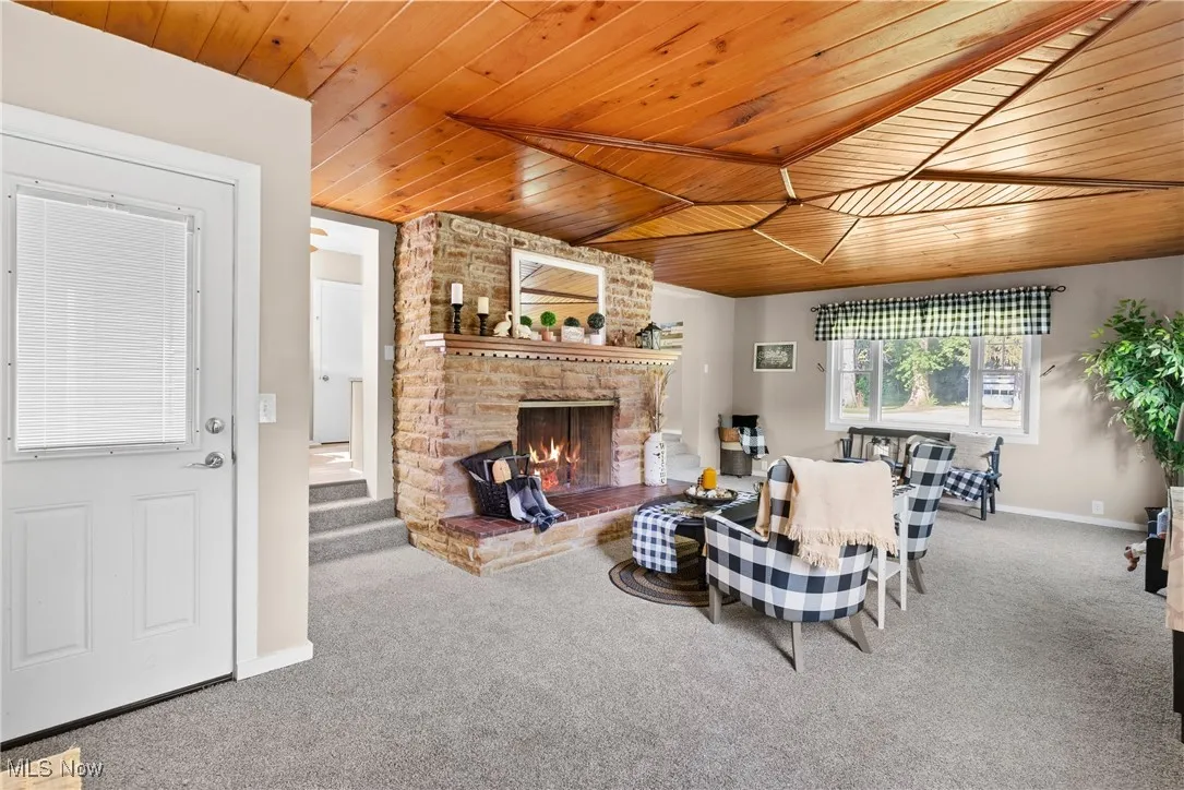 Living room featuring carpet floors, wood ceiling, and a brick fireplace