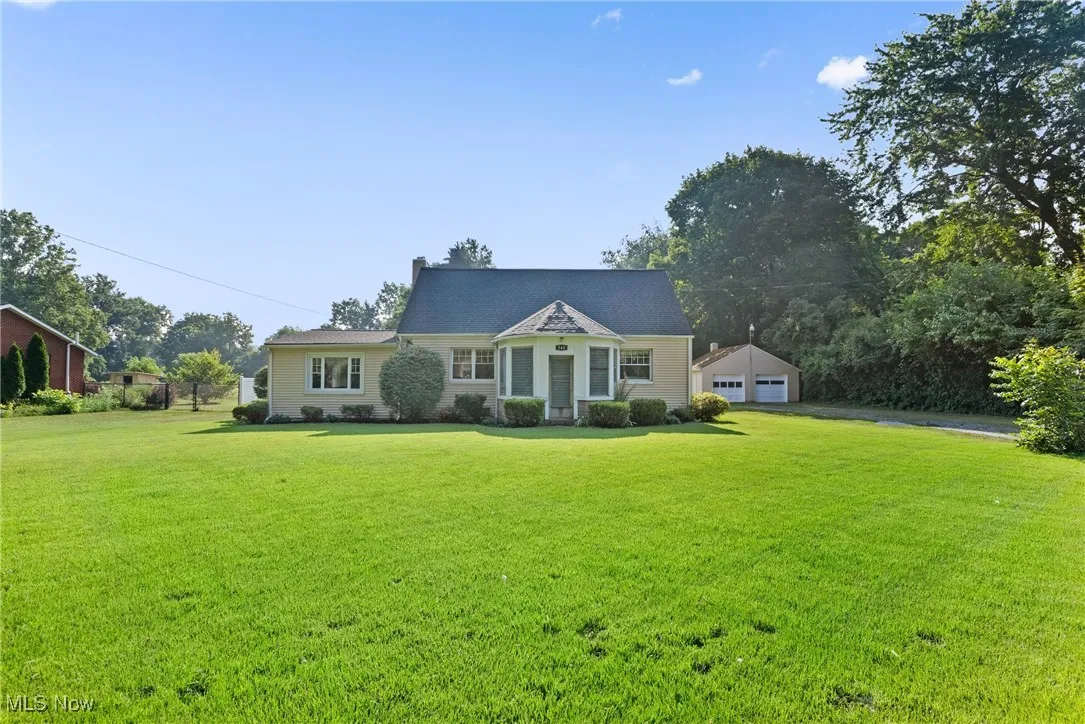 View of front of property with a front lawn, a detached garage, an outdoor structure, and a chimney