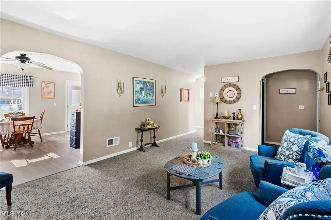 Carpeted living room with arched walkways and a ceiling fan