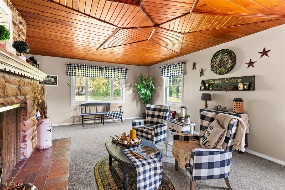 Living area with wooden ceiling, carpet flooring, and a stone fireplace