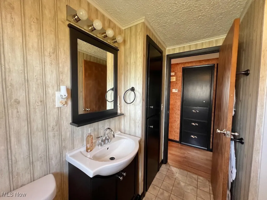 Bathroom with ornamental molding, vanity, tile patterned flooring, a textured ceiling, and wooden walls