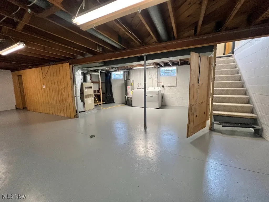 Basement featuring washer and dryer, stairs, heating unit, gas water heater, and concrete block wall