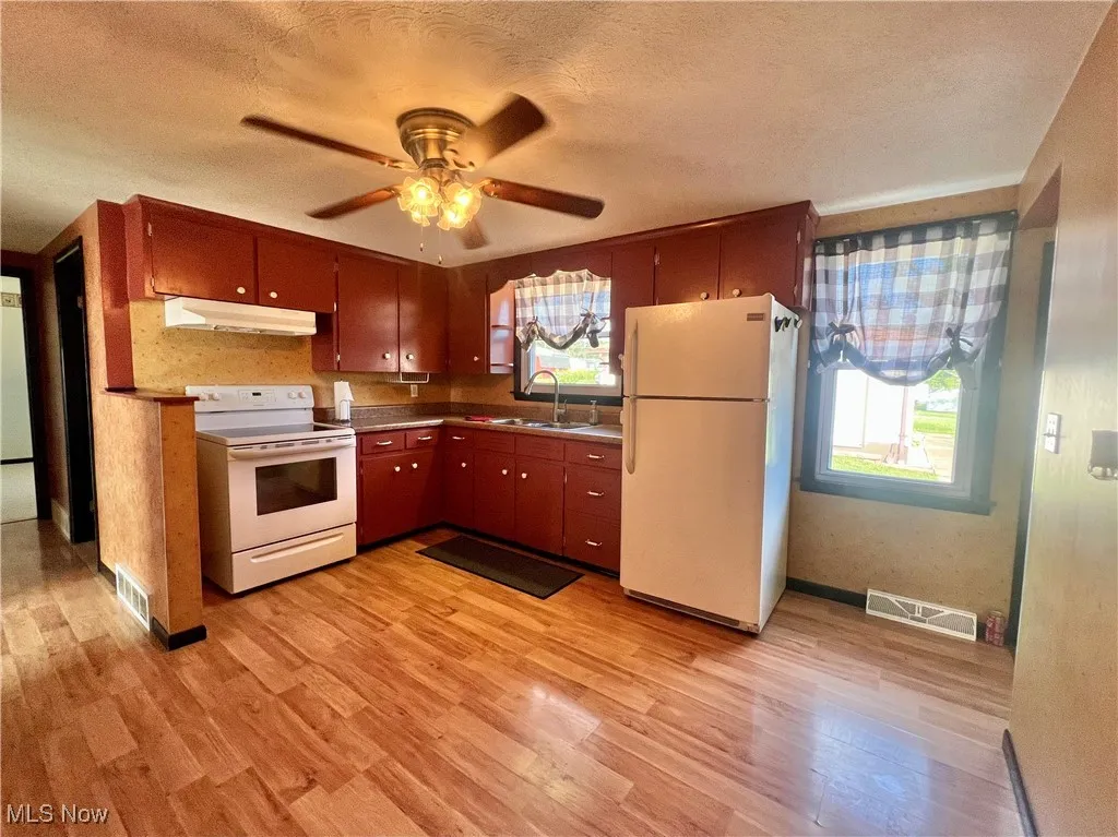 Kitchen with white appliances, light wood finished floors, plenty of natural light, and a textured ceiling