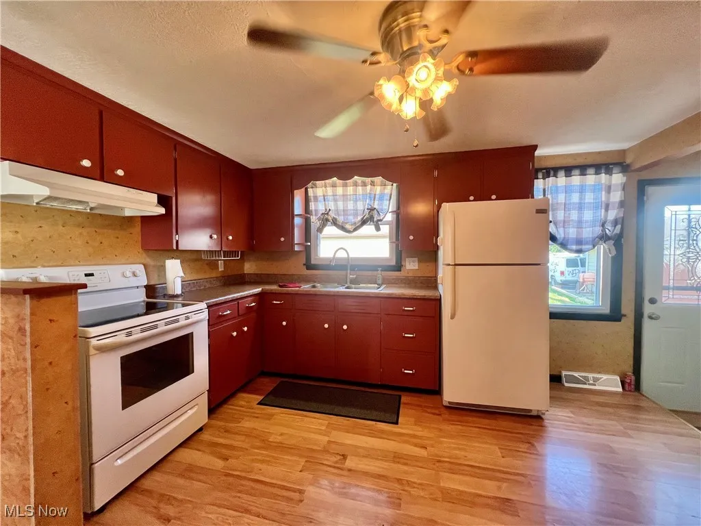 Kitchen featuring white appliances, under cabinet range hood, a ceiling fan, and light wood-style floors