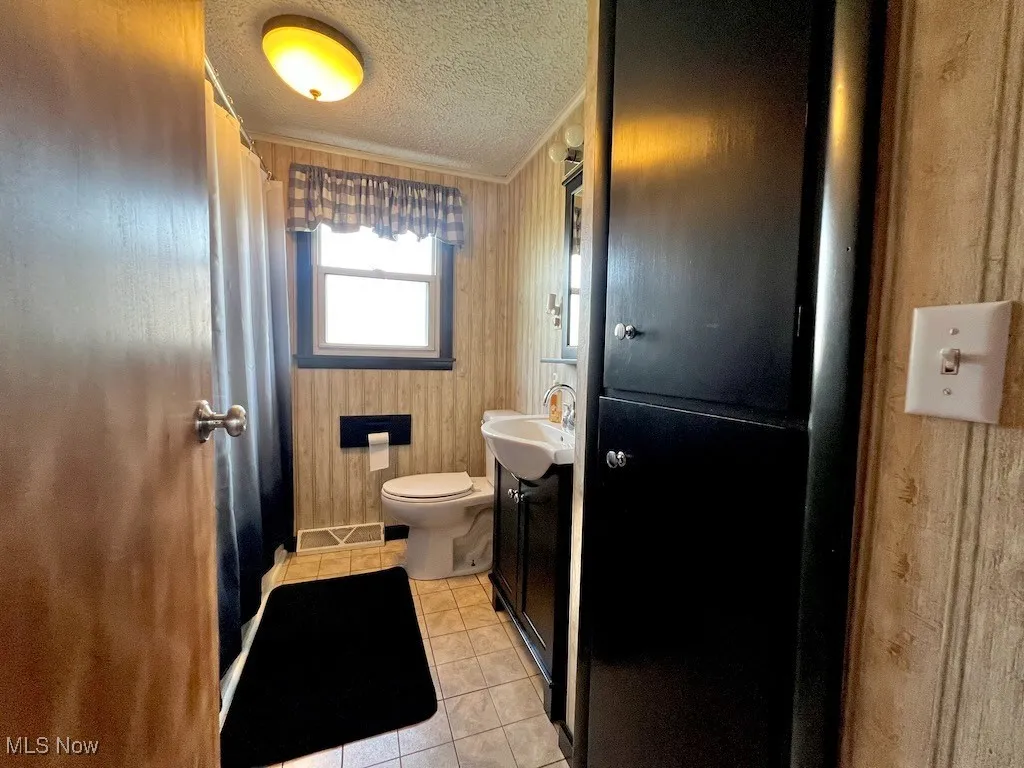 Full bathroom with tile patterned floors, a textured ceiling, curtained shower, and vanity