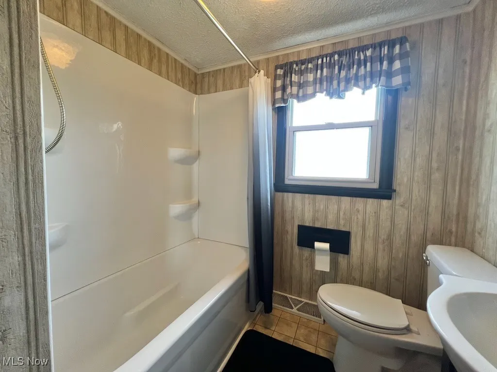 Bathroom featuring shower / bath combo with shower curtain, wooden walls, a textured ceiling, and tile patterned floors
