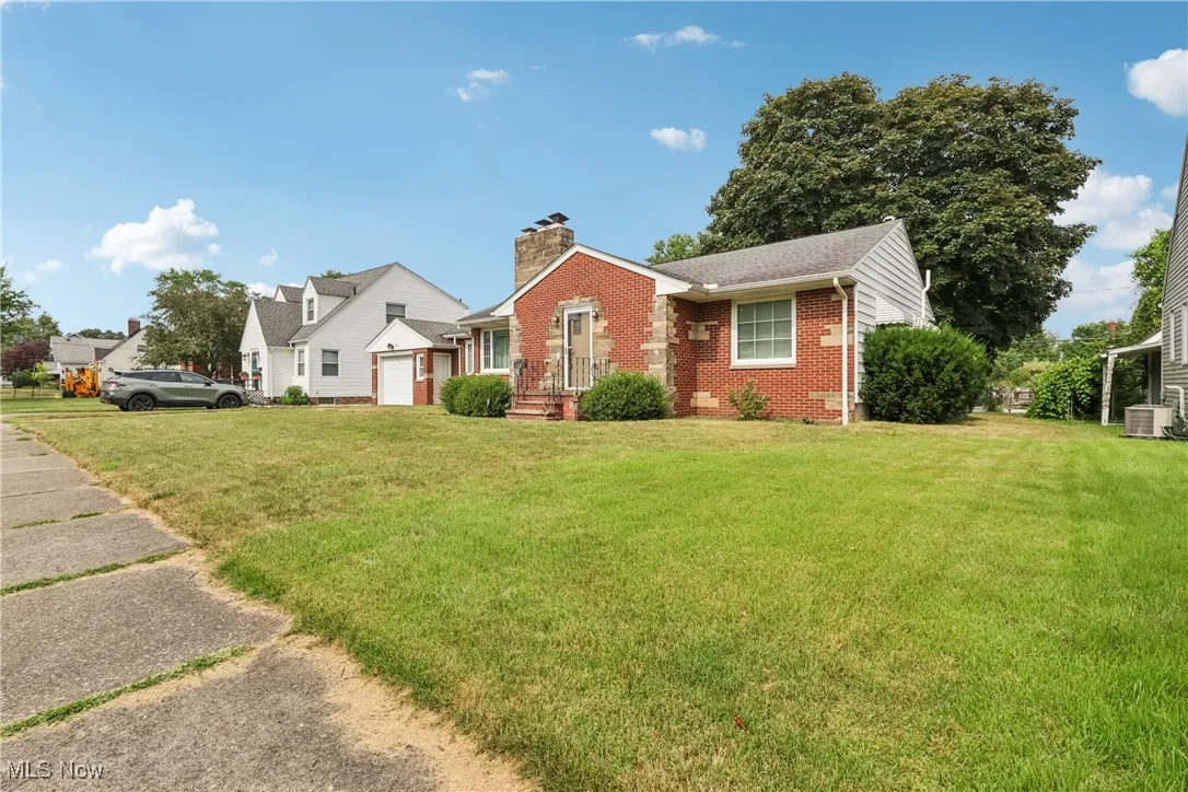 View of front facade featuring a front lawn, brick siding, a chimney, and an attached garage