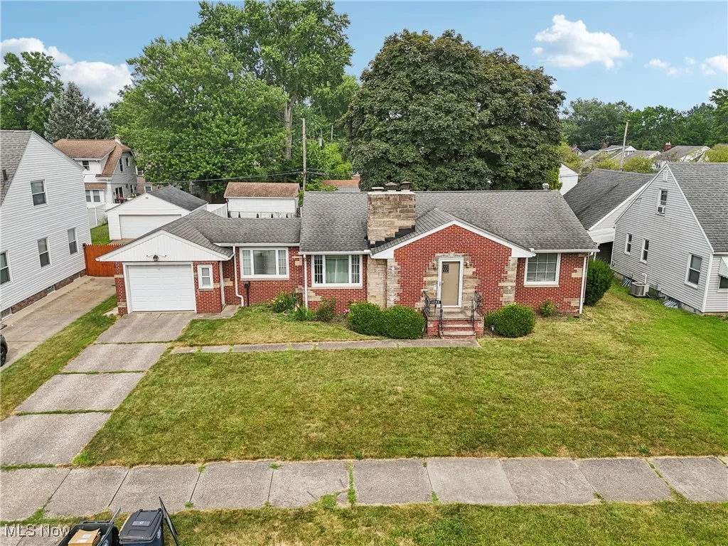 View of front facade featuring brick siding, driveway, a chimney, and a garage