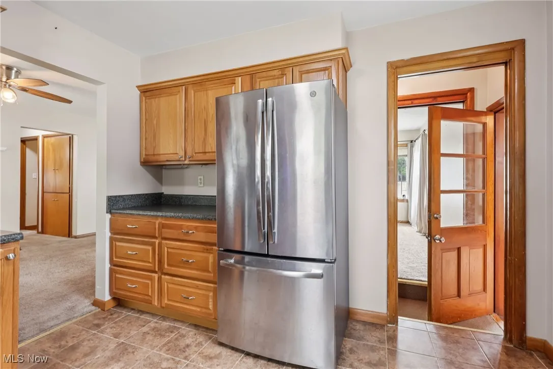 Kitchen featuring freestanding refrigerator, dark countertops, ceiling fan, brown cabinetry, and light carpet