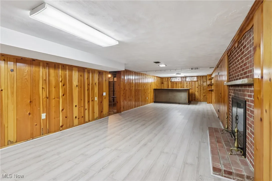 Unfurnished living room with a fireplace, wooden walls, and light wood-type flooring