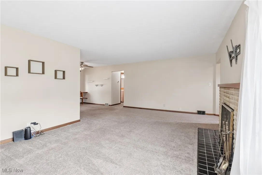 Unfurnished living room with a brick fireplace, carpet, and ceiling fan