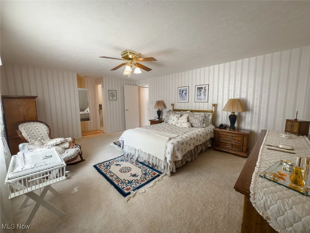 Primary bedroom featuring light carpet, ceiling fan, and a textured ceiling