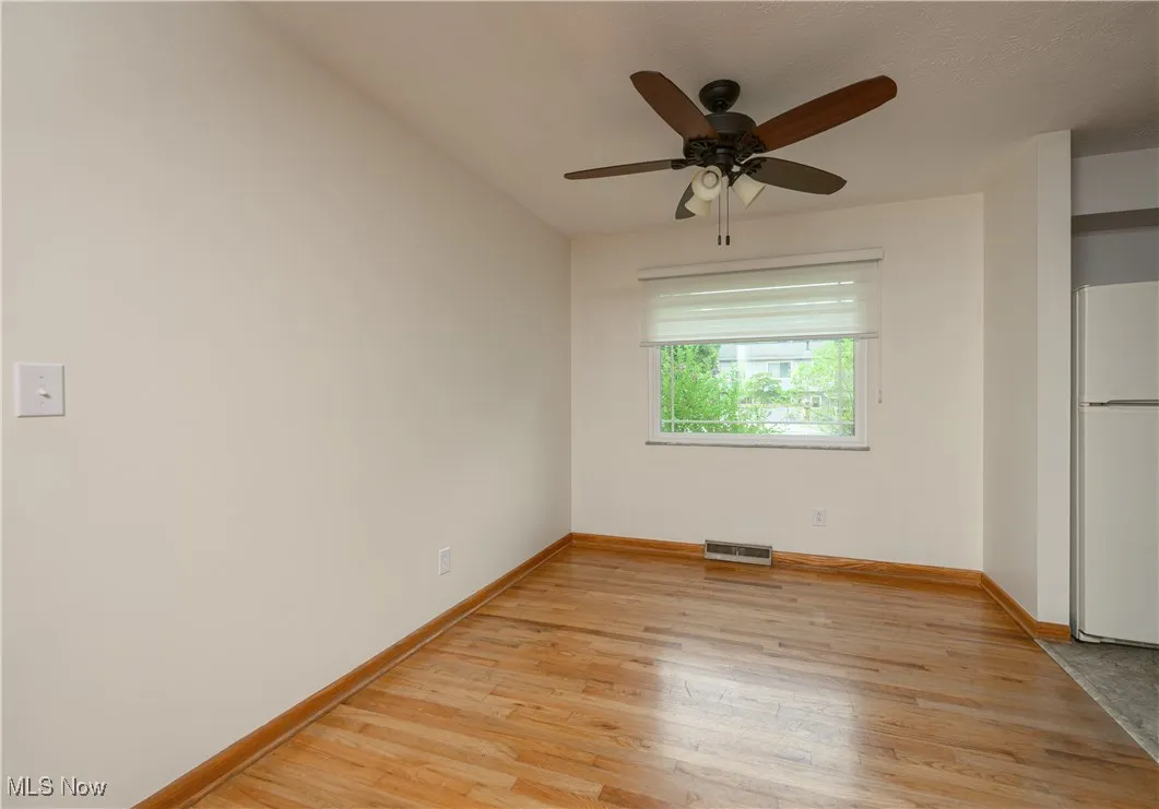 Unfurnished bedroom with freestanding refrigerator, light wood finished floors, and a ceiling fan