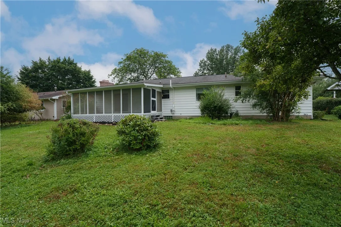 Back of house with a sunroom, a lawn, and a chimney
