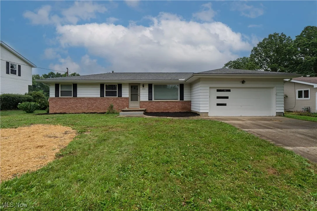 Single story home featuring a garage, driveway, brick siding, and a front yard