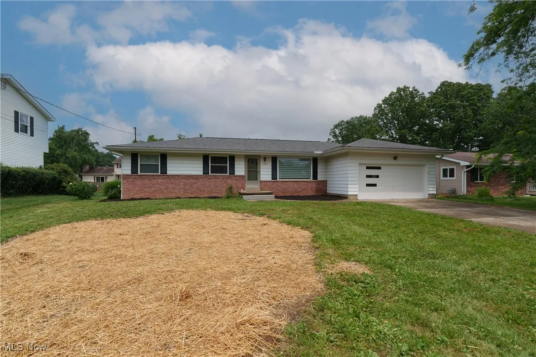 Single story home featuring a garage, concrete driveway, brick siding, and a front yard
