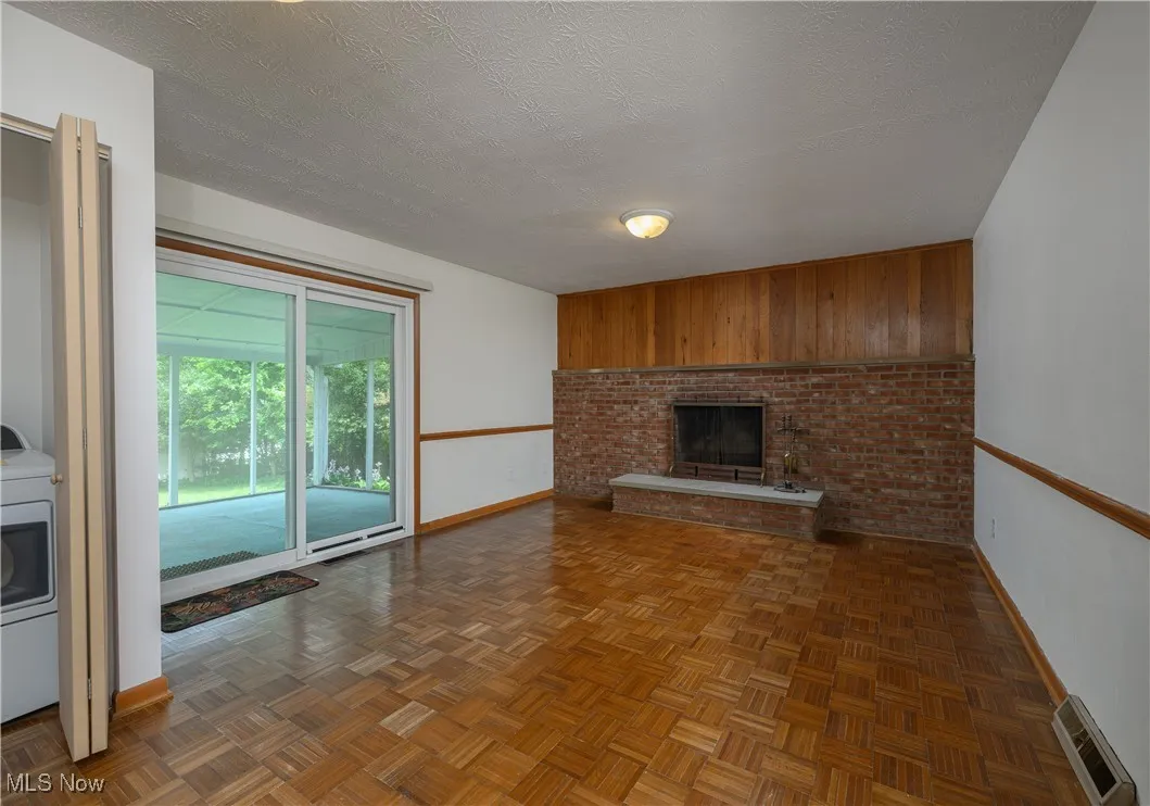 Unfurnished living room featuring a brick fireplace, washer / dryer, wooden walls, and a textured ceiling